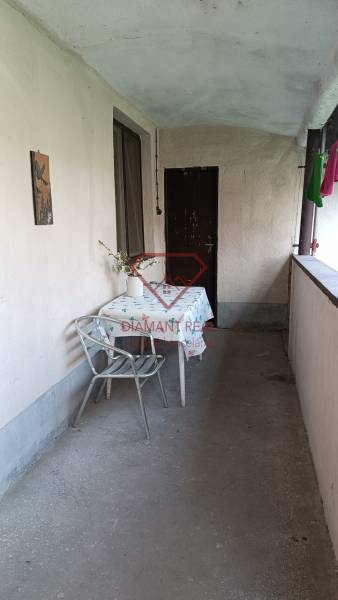 Zastřešená terasa rodinného domu, stůl se židlí, váza s květinami, obytný prostor.