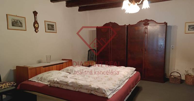 Ložnice v rodinném domě s dřevěným stropem, starožitnou skříní a klasickým lustrem.