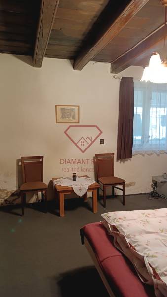 Pokoj v rodinném domě s dřevěným stropem, dvěma židlemi a stolkem.