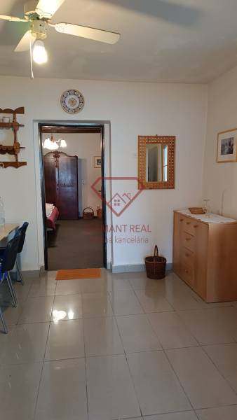 Interiér rodinného domu s dlažbou, dřevěnou komodou a stropním ventilátorem.