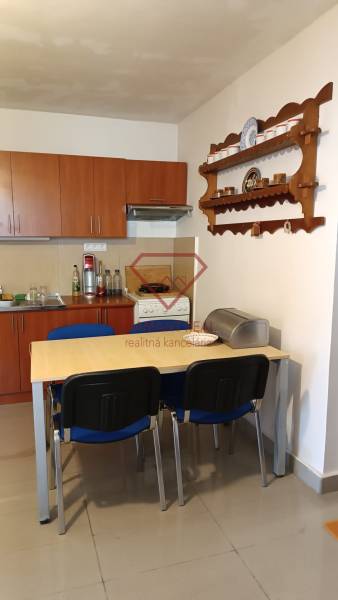 Jídelna v rodinném domě s kuchyňskou linkou, stolem a policí na stěně.