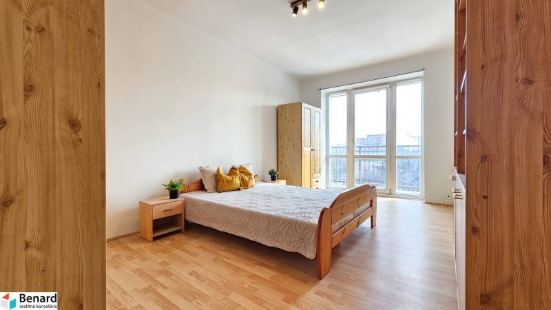 Ložnice v 2-pokojovém bytě s podlahou s dřevěným dekorem a velkými okny.
