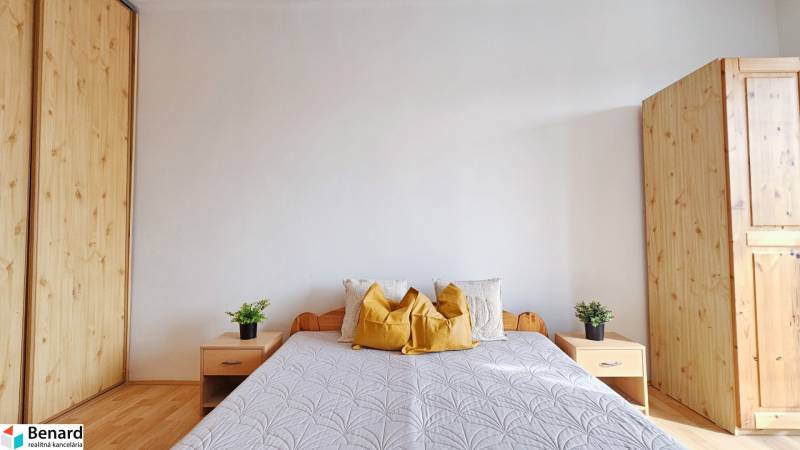 Ložnice s dřevěnými skříněmi a postelí v 2pokojovém bytě, podlaha s dřevěným dekorem.