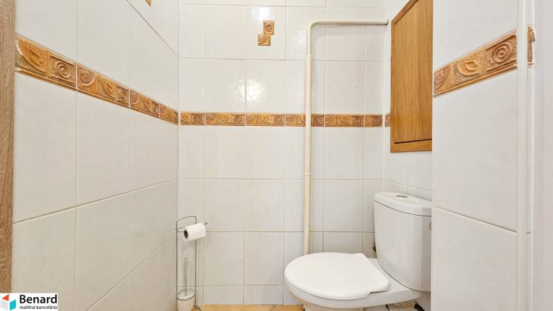 Koupelna s toaletou v 2-pokojovém bytě se světlými dlaždicemi a dřevěným dekorem.