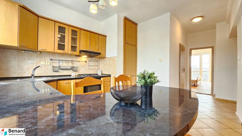 Kuchyně s dřevěnými skříňkami, pultem a výhledem do pokoje v 2pokojovém bytě.