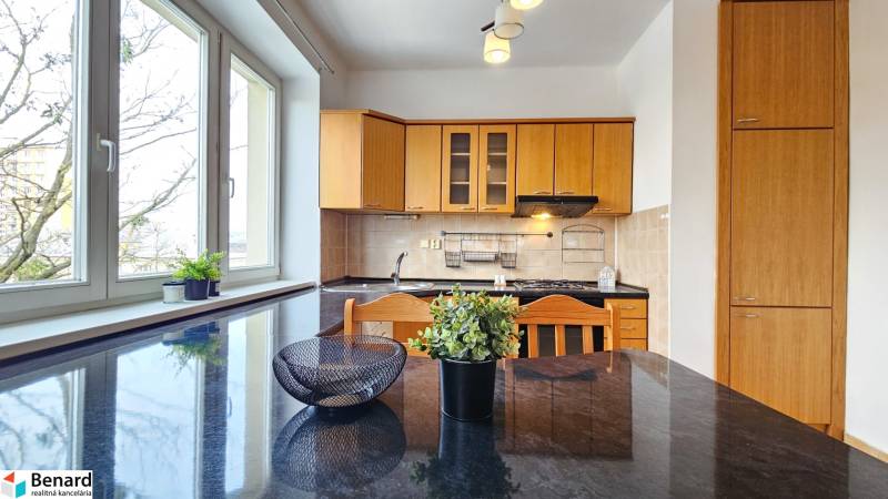 Kuchyně s dřevěnými skříňkami a černou pracovní deskou v 2-pokojovém bytě.