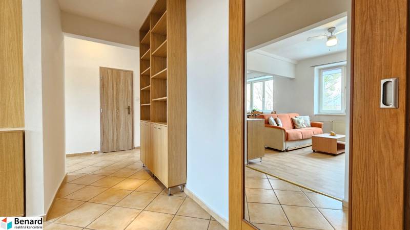 Chodba v 2-pokojovém bytě s dlažbou, vestavěnou skříní a výhledem do obývacího pokoje.