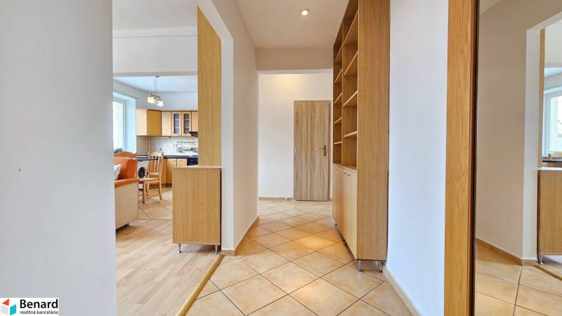 Chodba v 2-pokojovém bytě s podlahou s dřevěným dekorem a kuchyní v pozadí.