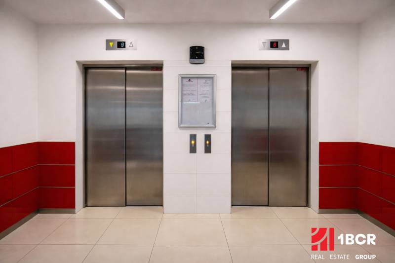 Dva výtahy se šedými dveřmi a bílými stěnami s červenými obklady.