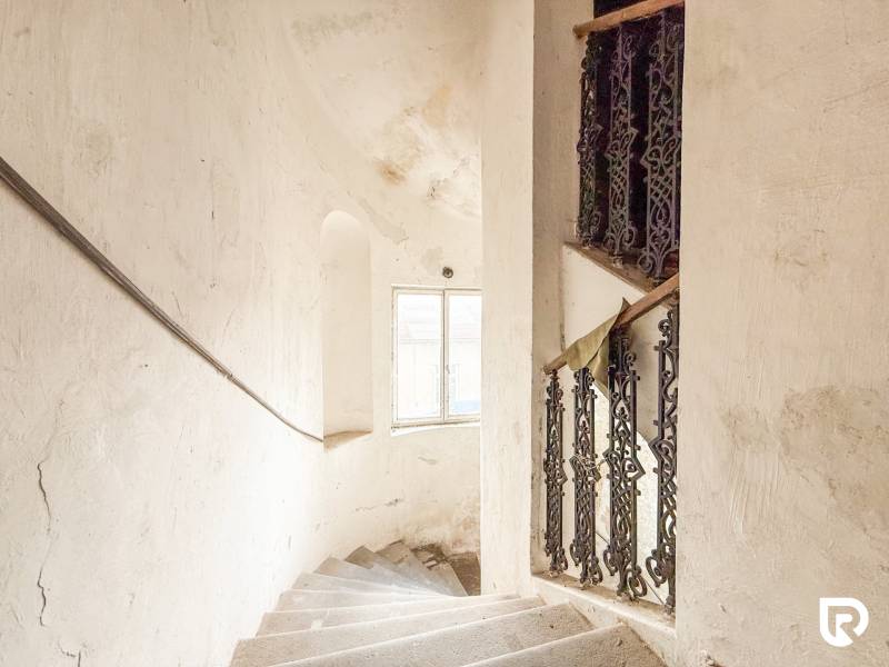 Schodiště v rodinném domě s oknem a ozdobným zábradlím, bílá stěna s patinou.