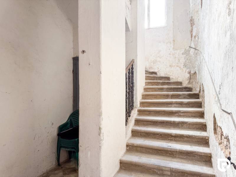 Schodiště v rodinném domě s hromadou plastových židlí. Opotřebované stěny.