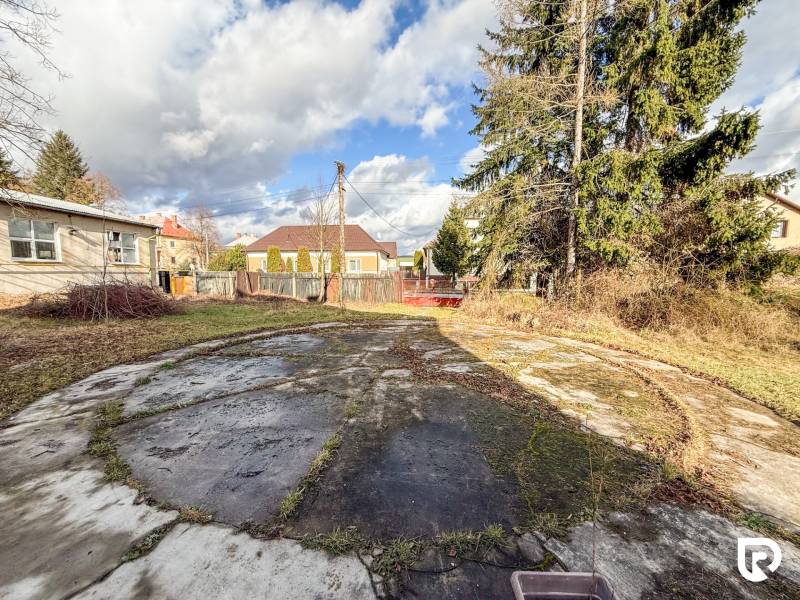 Rodinný dům v obci Bobot, na ulici Bobot, s betonovou plochou a dřevinami v zahradě.