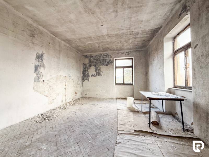 Opuštěná místnost s poškozenými stěnami a podlahou s dřevěným dekorem v rodinném domě.