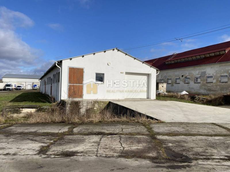 Exteriér skladů a hal v Rybkách s bílou fasádou a dřevěnými dveřmi.