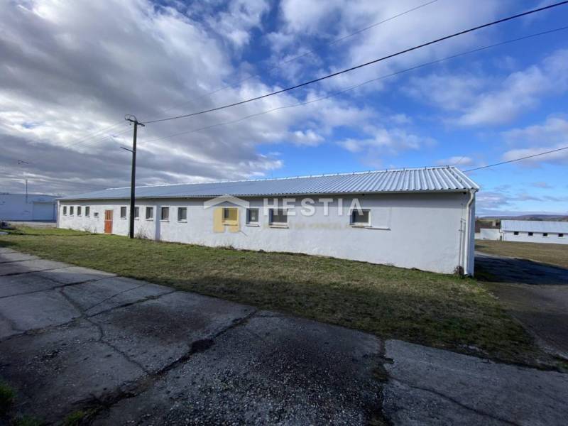 Bílá budova skladů a hal v Rybkách, obklopená trávou a betonovým chodníkem.