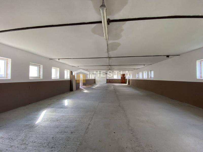 Prostorný interiér skladu a haly s okny na obou stranách, betonová podlaha.