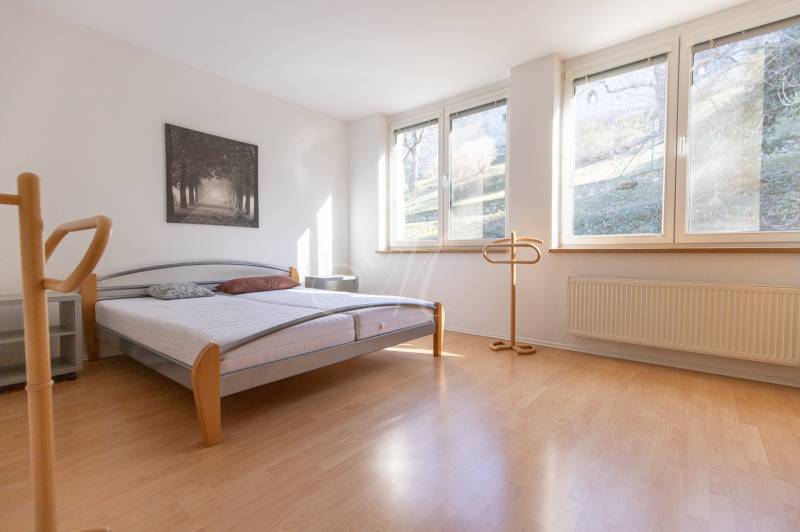 Světlá ložnice s postelí a podlahou s dřevěným dekorem ve 3-pokojovém bytě.