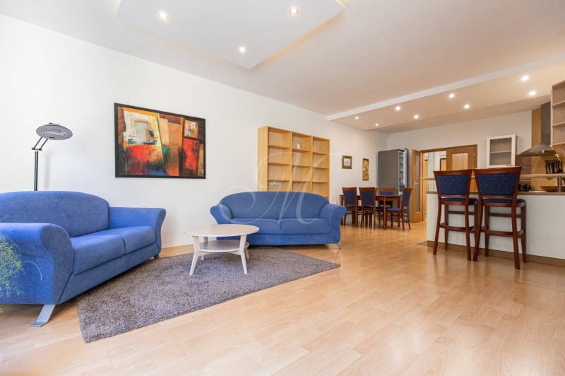 Obývací pokoj s modrými sedačkami, barevným obrazem a podlahou s dřevěným dekorem ve 3pokojovém bytě.