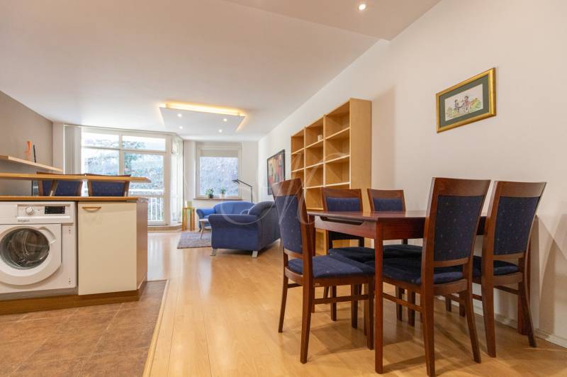 Obývací pokoj s podlahou s dřevěným dekorem, jídelním stolem a pračkou ve 3pokojovém bytě.