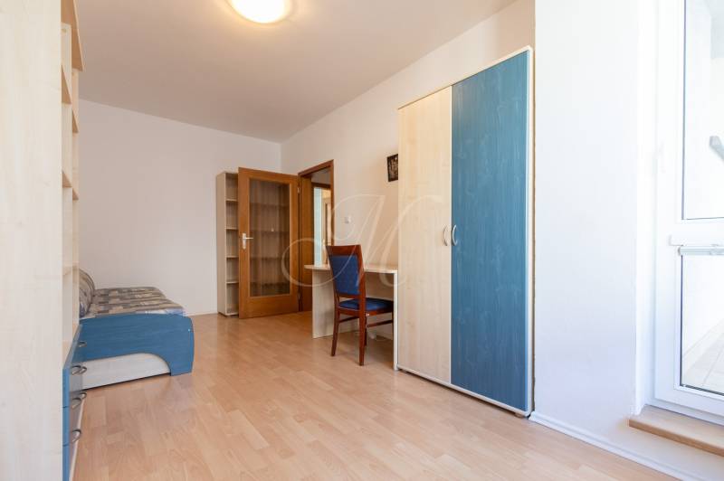 Pokoj v 3-pokojovém bytě s podlahou s dřevěným dekorem, skříní a pohovkou.