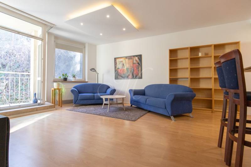 Obývací pokoj v 3pokojovém bytě s modrými sedačkami a podlahou s dřevěným dekorem.