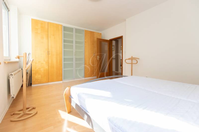 Světlá ložnice ve 3-pokojovém bytě s podlahou s dřevěným dekorem a prostornou skříní.