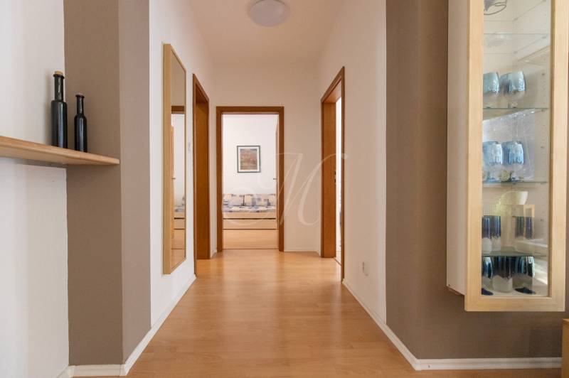 Chodba ve 3-pokojovém bytě s podlahou s dřevěným dekorem, zrcadlem a skleněnou vitrínou.