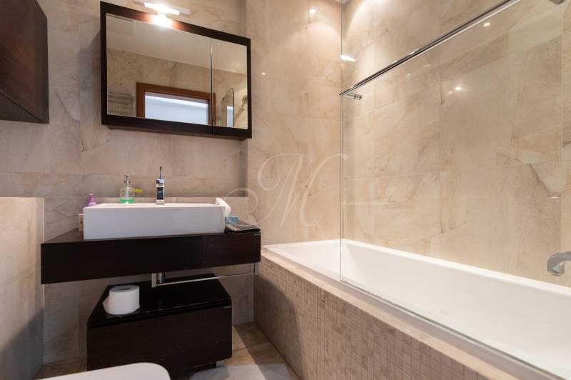 Koupelna s vanou a tmavým nábytkem v 2pokojovém bytě, světlé obklady.