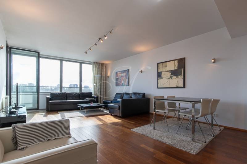 Obývací pokoj s velkými okny, podlaha s dřevěným dekorem, pohodlný nábytek a jídelní kout.