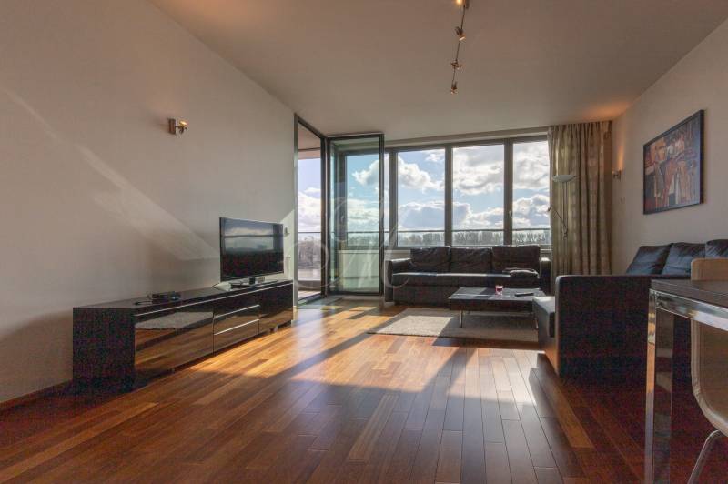 Obývací pokoj v dvoupokojovém bytě s podlahou s dřevěným dekorem a velkými okny.