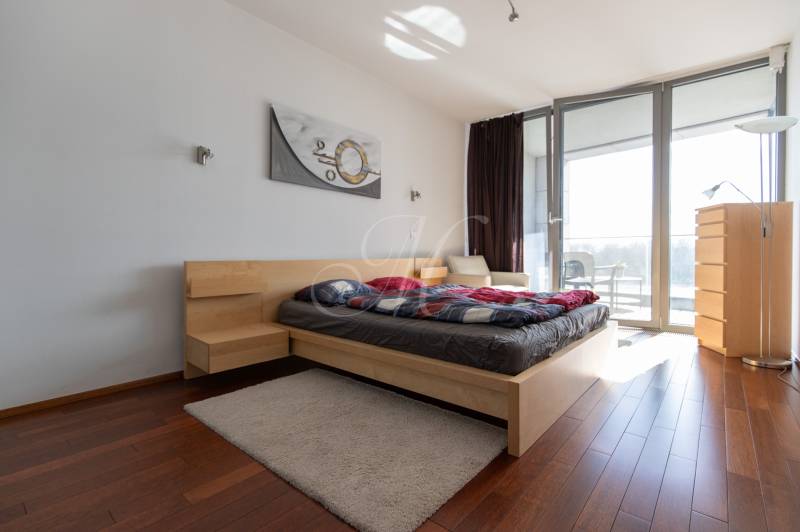 Ložnice v dvoupokojovém bytě s podlahou s dřevěným dekorem a prostornými okny.