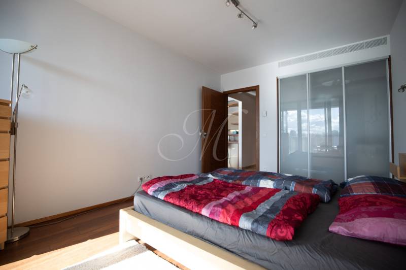 Ložnice ve dvoupokojovém bytě s podlahou s dřevěným dekorem, postelí a skříní.