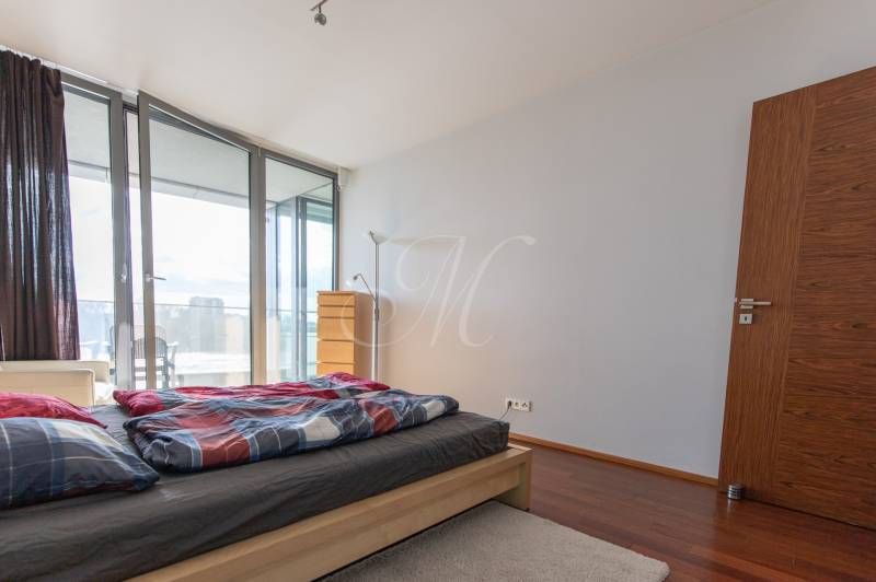 Ložnice v 2pokojovém bytě s podlahou s dřevěným dekorem a přístupem na balkon.