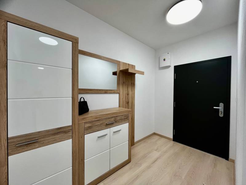 Chodba s podlahou s dřevěným dekorem v 2-pokojovém bytě, moderní nábytek a tmavé dveře.