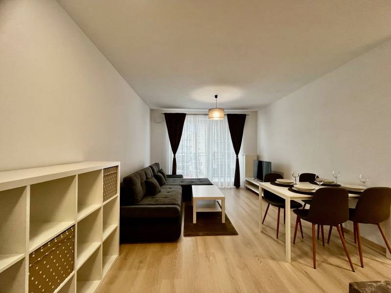 Obývací pokoj v 2-pokojovém bytě s pohovkou a jídelním stolem, podlaha s dřevěným dekorem.