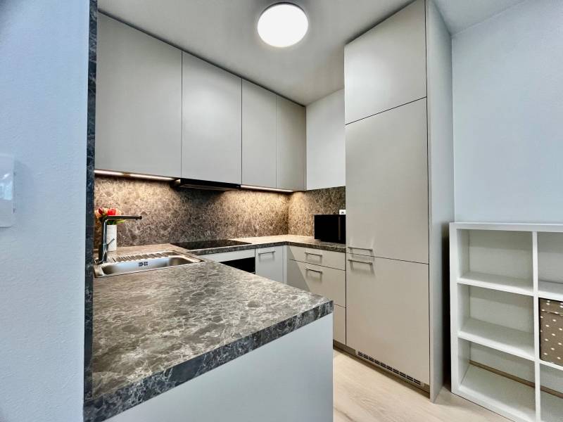 Kuchyně v 2pokojovém bytě s kamennou pracovní deskou a bílými skříňkami.