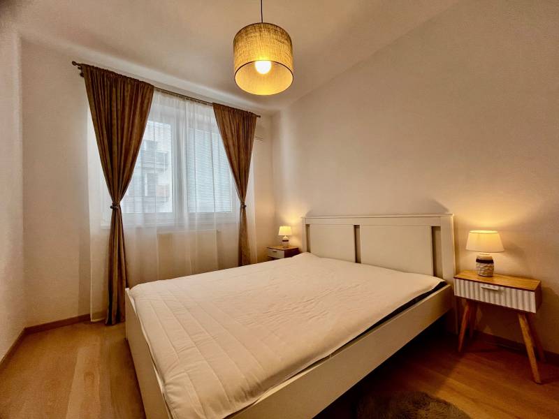 Ložnice s velkou postelí, závěsy a podlahou s dřevěným dekorem v 2-pokojovém bytě.