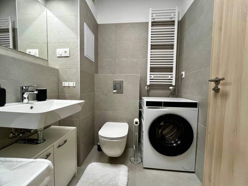 Koupelna v 2-pokojovém bytě s umyvadlem, pračkou a toaletou, moderní obklady.