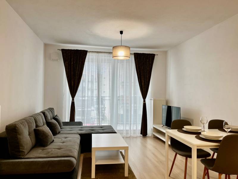 Obývací pokoj v 2-pokojovém bytě s pohovkou, jídelním stolem a podlahou s dřevěným dekorem.