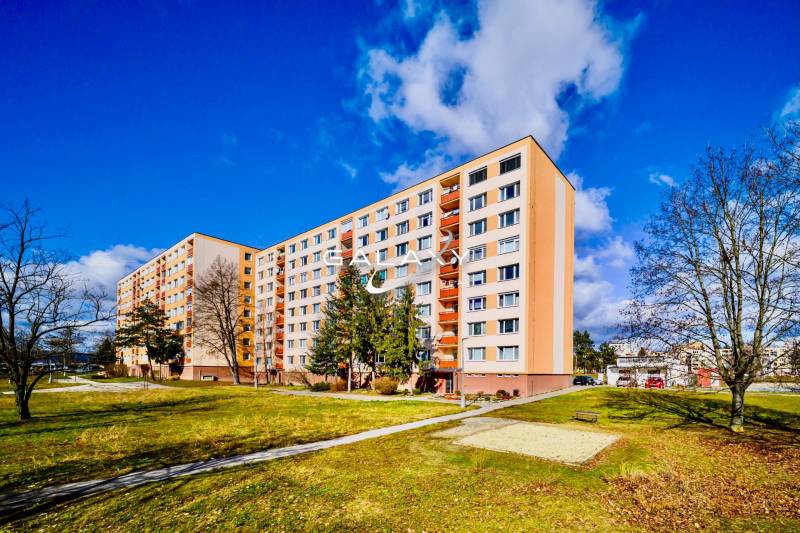 Panelový dům na sídlišti Rúbanisko II v Lučenci obklopený zelení a lavičkami.