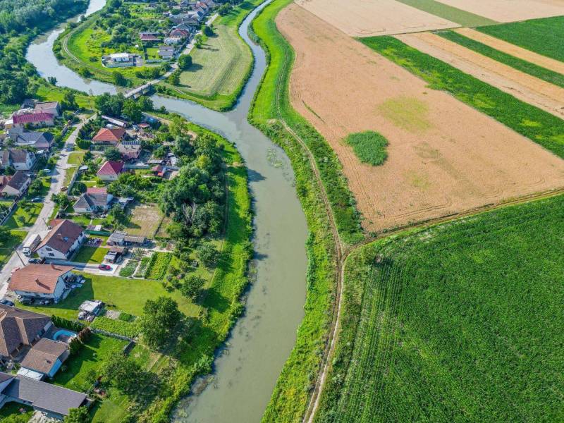 Řeka obklopená vesnicí a poli v Černé Vodě se zemědělskými a lesními pozemky.