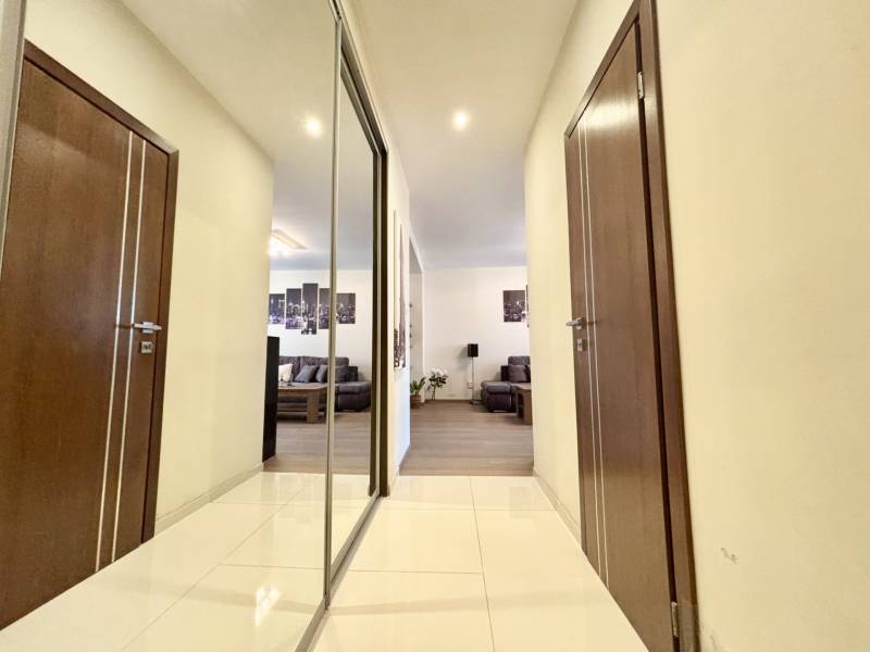 Chodba v 2-pokojovém bytě s dlažbou, zrcadlem a výhledem do obývacího pokoje.