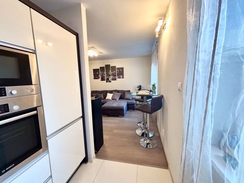 Kuchyňský kout se spotřebiči, barovým sezením a výhledem na obývací pokoj v 2pokojovém bytě.