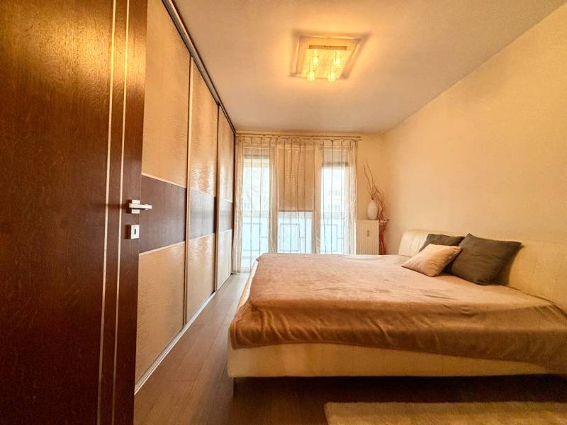 Ložnice v 2pokojovém bytě s velkou postelí a podlahou s dřevěným dekorem.