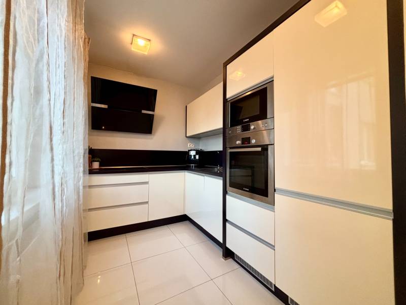 Bílá kuchyně s černými akcenty a spotřebiči v 2pokojovém bytě.