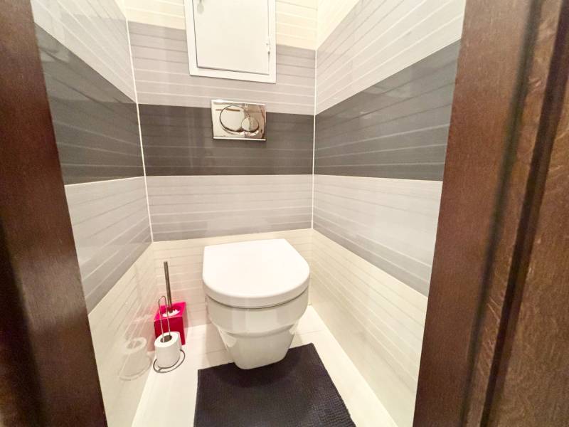 Toaleta v 2-pokojovém bytě s bílými a šedými dlaždicemi na stěnách.