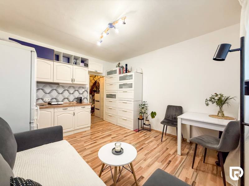 Garsonka s kuchyňskou linkou, stolkem a podlahou s dřevěným dekorem.