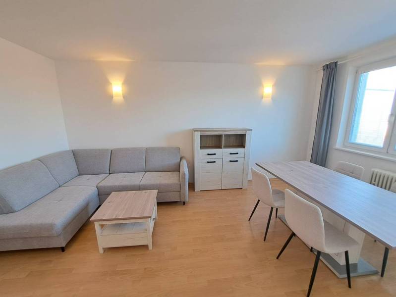 Obývací pokoj ve 4pokojovém bytě s rohovou sedačkou a jídelním stolem.