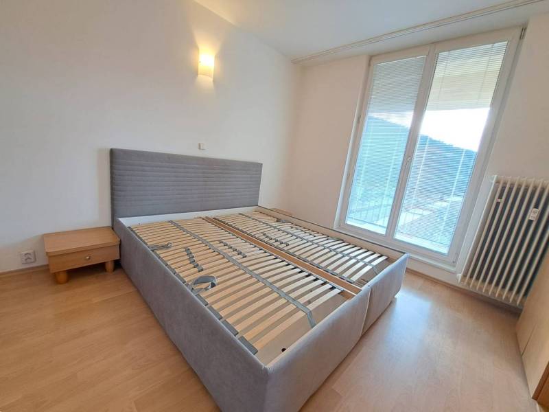 Ložnice ve 4pokojovém bytě s postelí a nočním stolkem, podlaha s dřevěným dekorem.