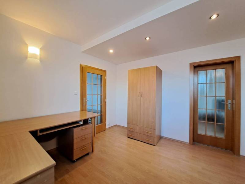 Pokoj ve 4pokojovém bytě s podlahou s dřevěným dekorem, stolem a skříní.